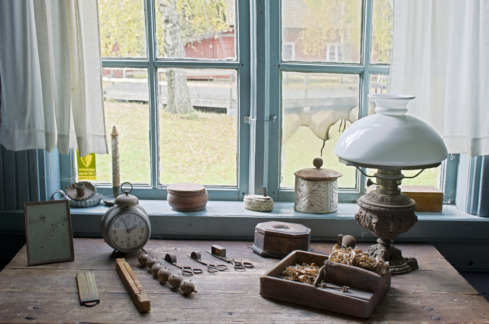 Ett bord med gamla föremål, bland annat en oljelampa, invid ett fönster på Ingå Gammelgård.